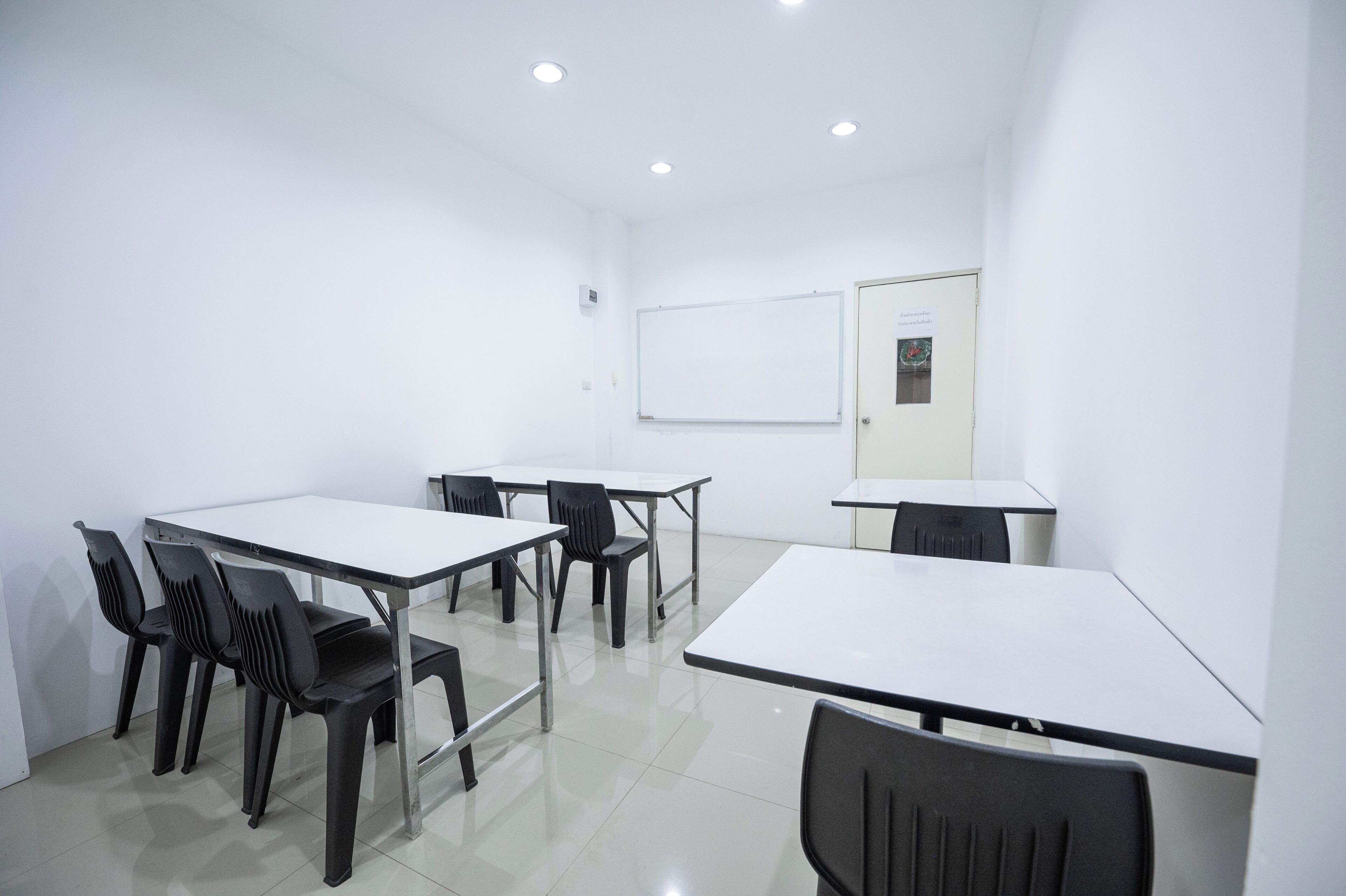 A conference room with white tables and chairs, a whiteboard, and a door with a poster.