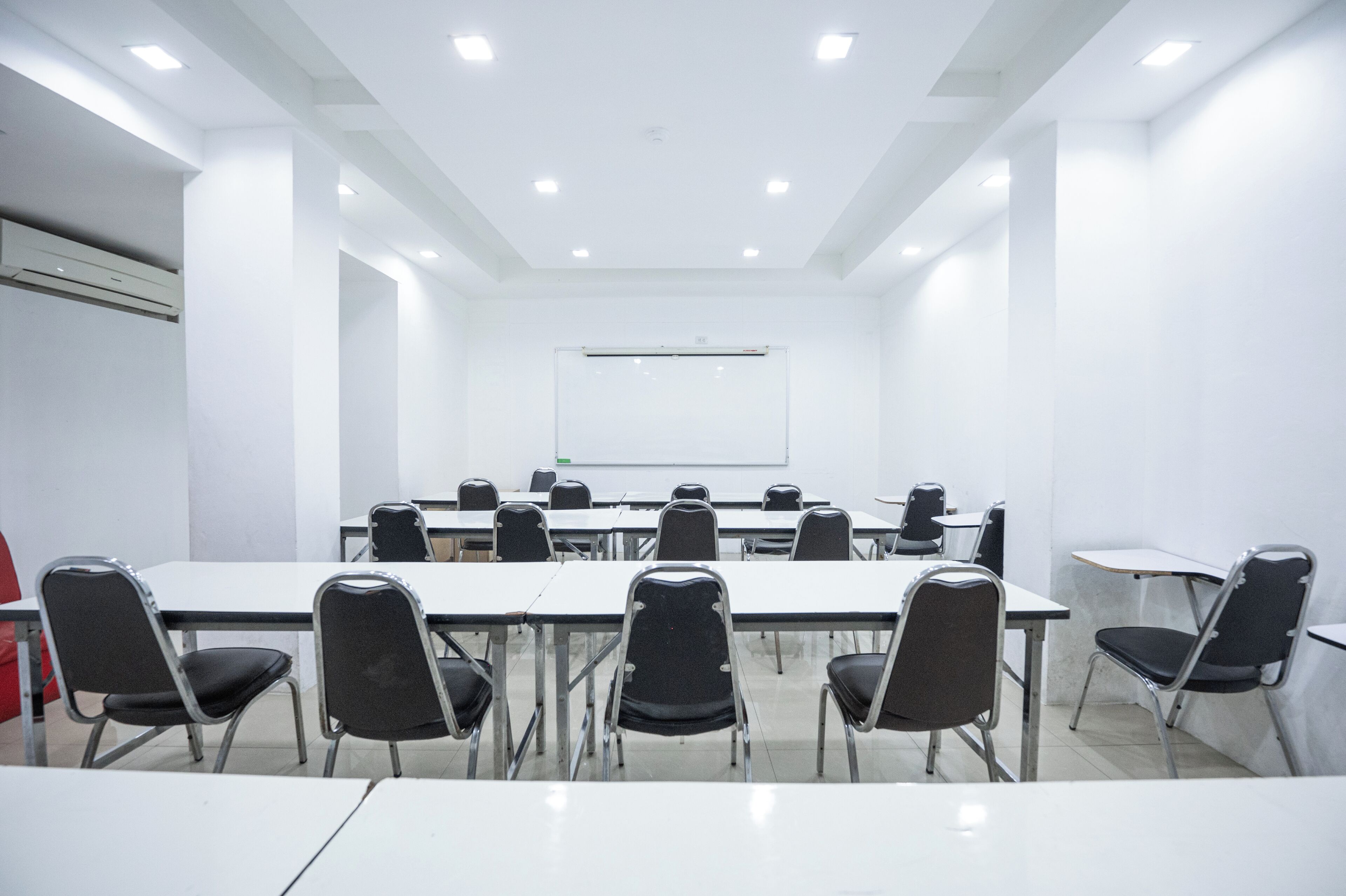 A conference room with white walls, a whiteboard, and multiple tables and chairs.
