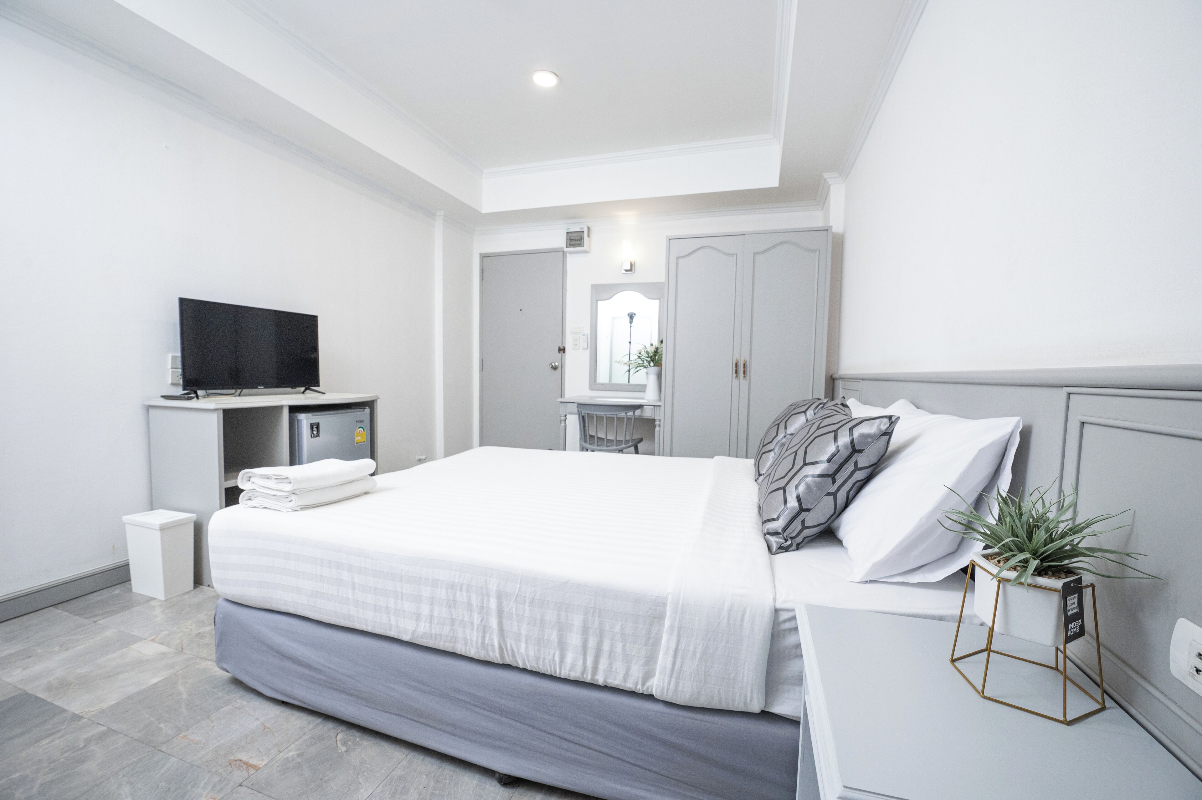 Ein modernes Hotelzimmer mit einem ordentlich bezogenen Bett, einem Fernseher, einem kleinen Schreibtisch und einer Topfpflanze.