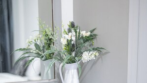 Ein weißes Schminktischchen mit Spiegel, eine weiße Vase mit weißen Blumen und ein weißer Stuhl.