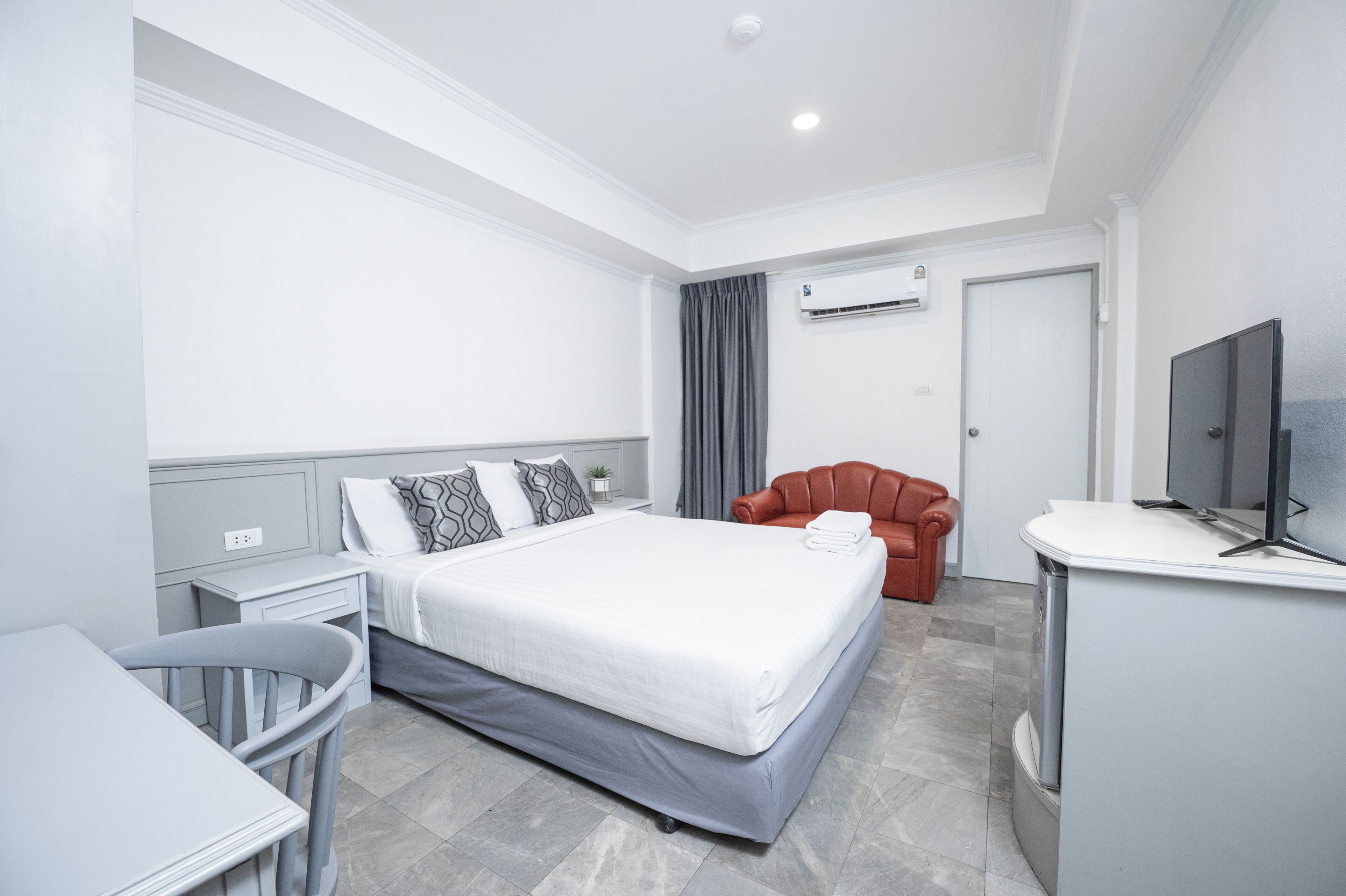 Een moderne hotelkamer met een groot bed, een bureau, een stoel, een televisie en een airconditioner.