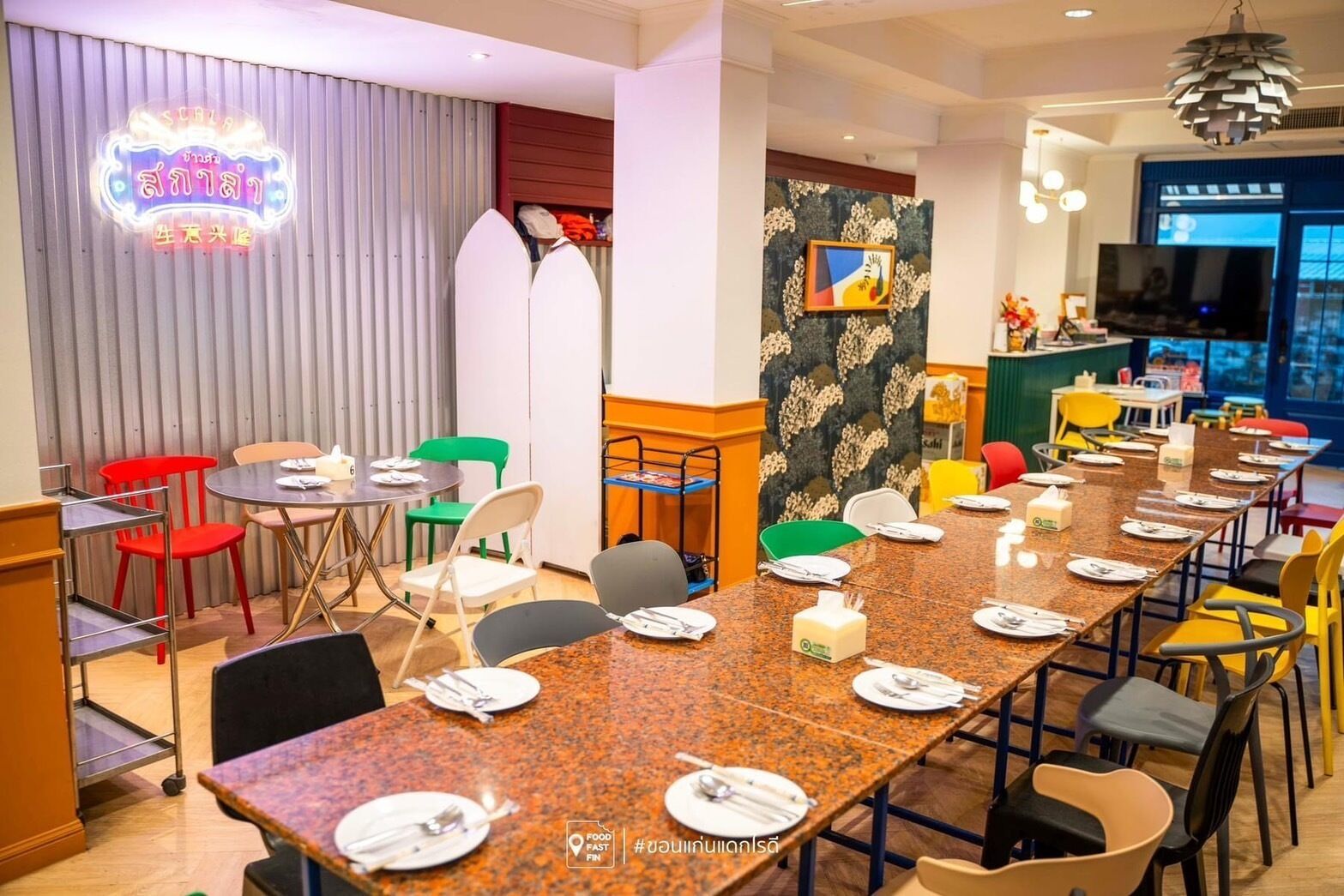 A dining area with a long table set for a meal, surrounded by colorful chairs.