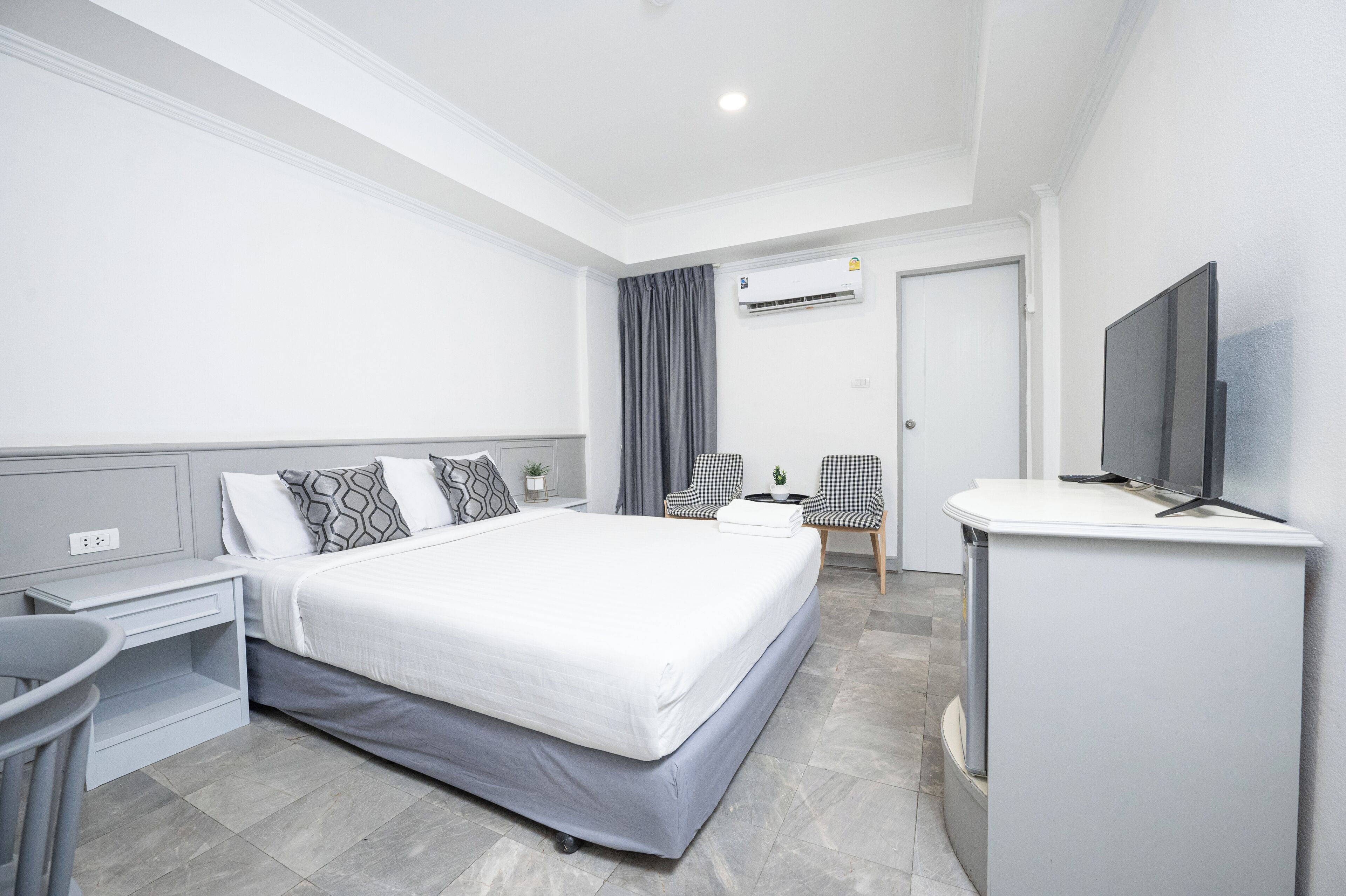 A modern hotel room with a large bed, a desk, a chair, a TV, and an air conditioning unit.