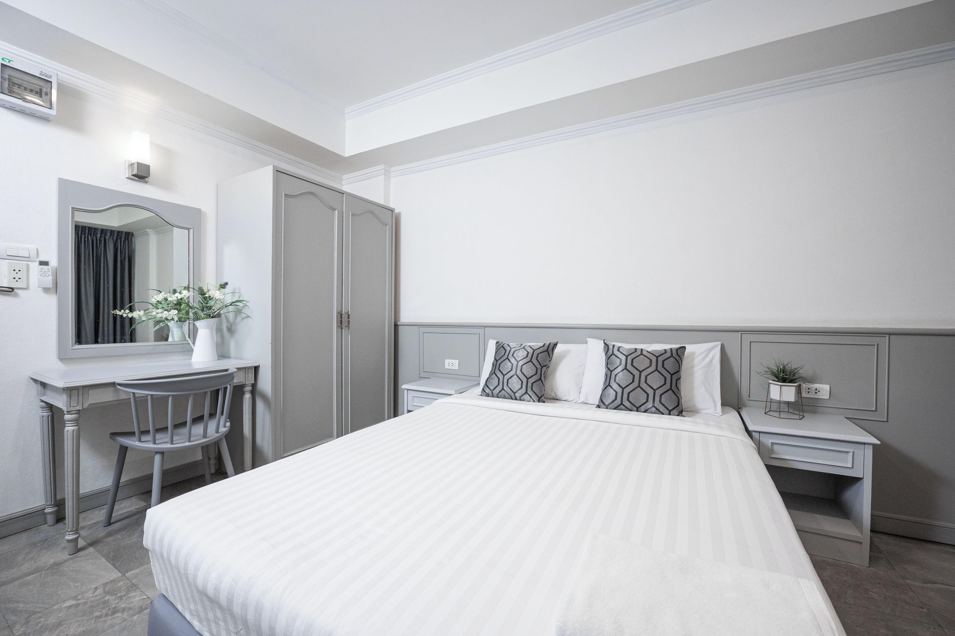 Habitación de hotel con una cama grande, un escritorio con una silla, un espejo y una mesita de noche con una planta.