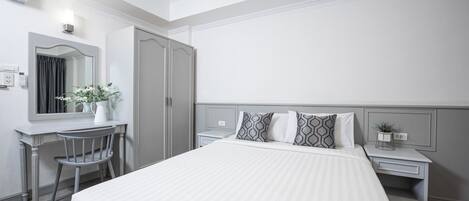 Habitación de hotel con una cama grande, un escritorio con una silla, un espejo y una mesita de noche con una planta.