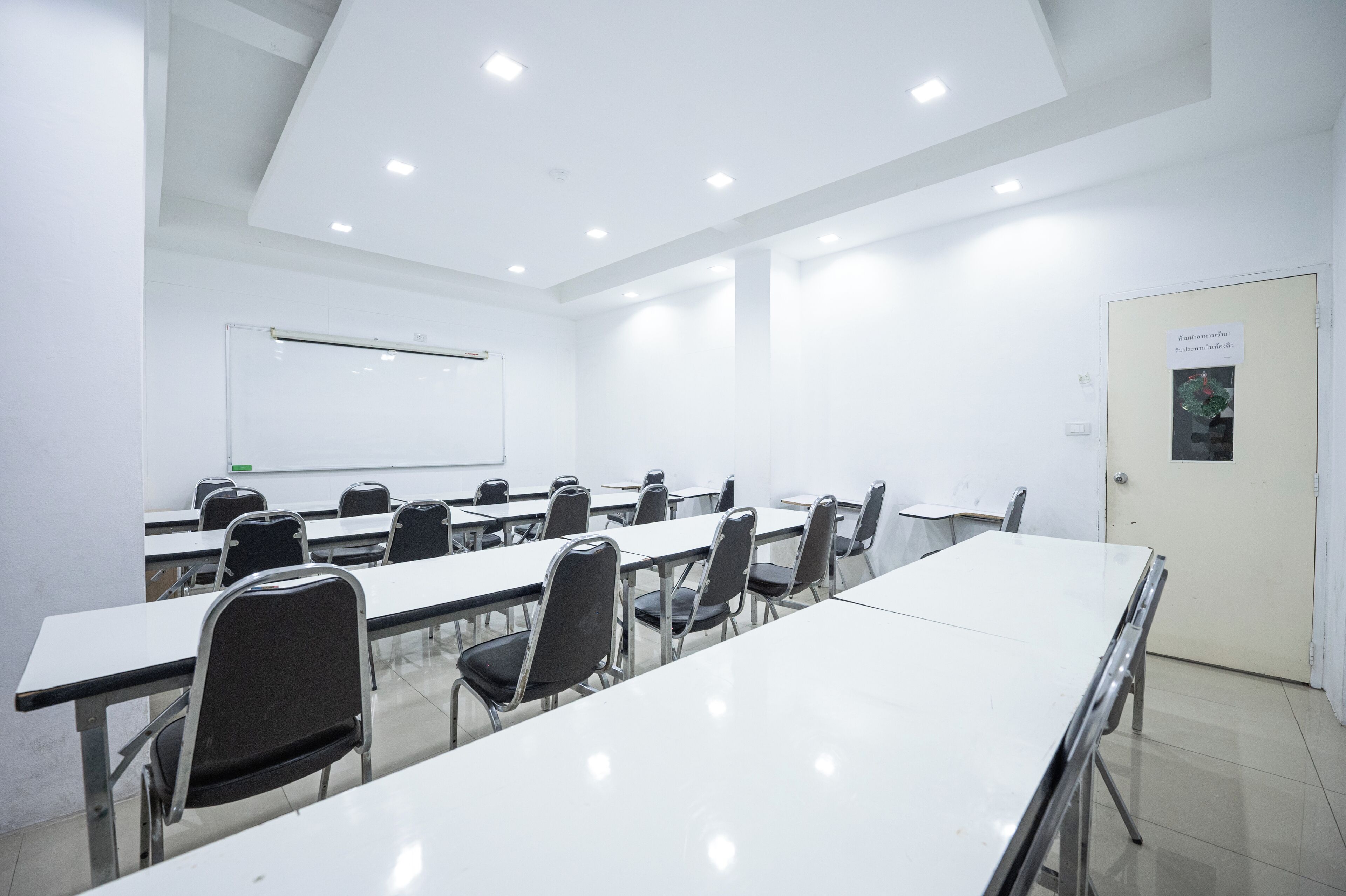 Une salle de conférence avec des tables et des chaises blanches, un tableau blanc et une porte avec une pancarte.