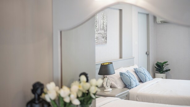 Ein Schlafzimmer mit Bett, Nachttisch, Lampe und einem Spiegel, der den Blick aus dem Fenster reflektiert.