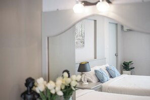 A bedroom with a bed, bedside table, lamp, and a mirror reflecting a window view. - Chaipat Hotel (Khon Kaen)