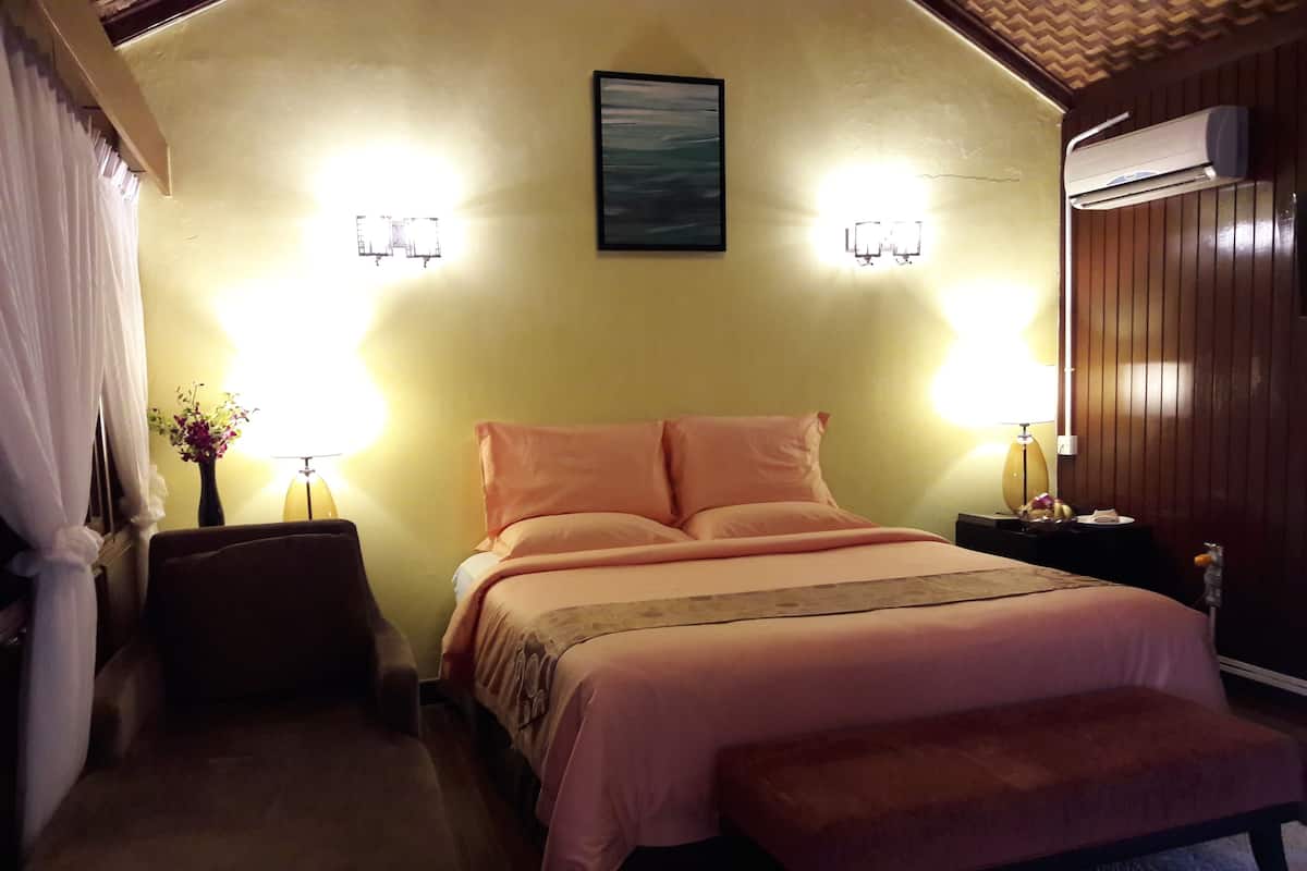 A bedroom with a bed, bedside tables, a nightstand, a bench, and a wall-mounted air conditioner.