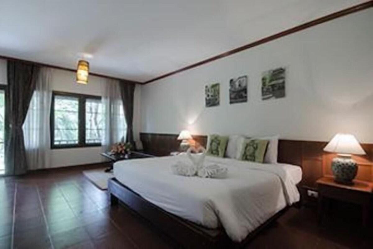 A hotel room with a large bed, a nightstand with a lamp, and a window with curtains.