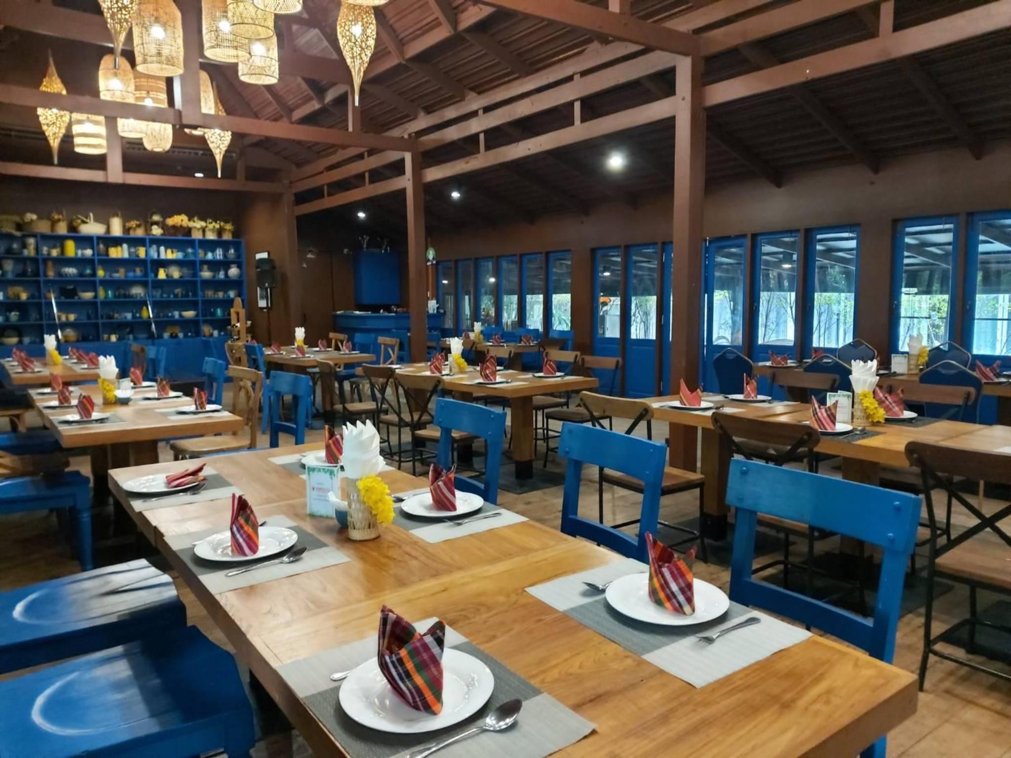 A restaurant with wooden tables and blue chairs, arranged in a spacious layout with large windows.