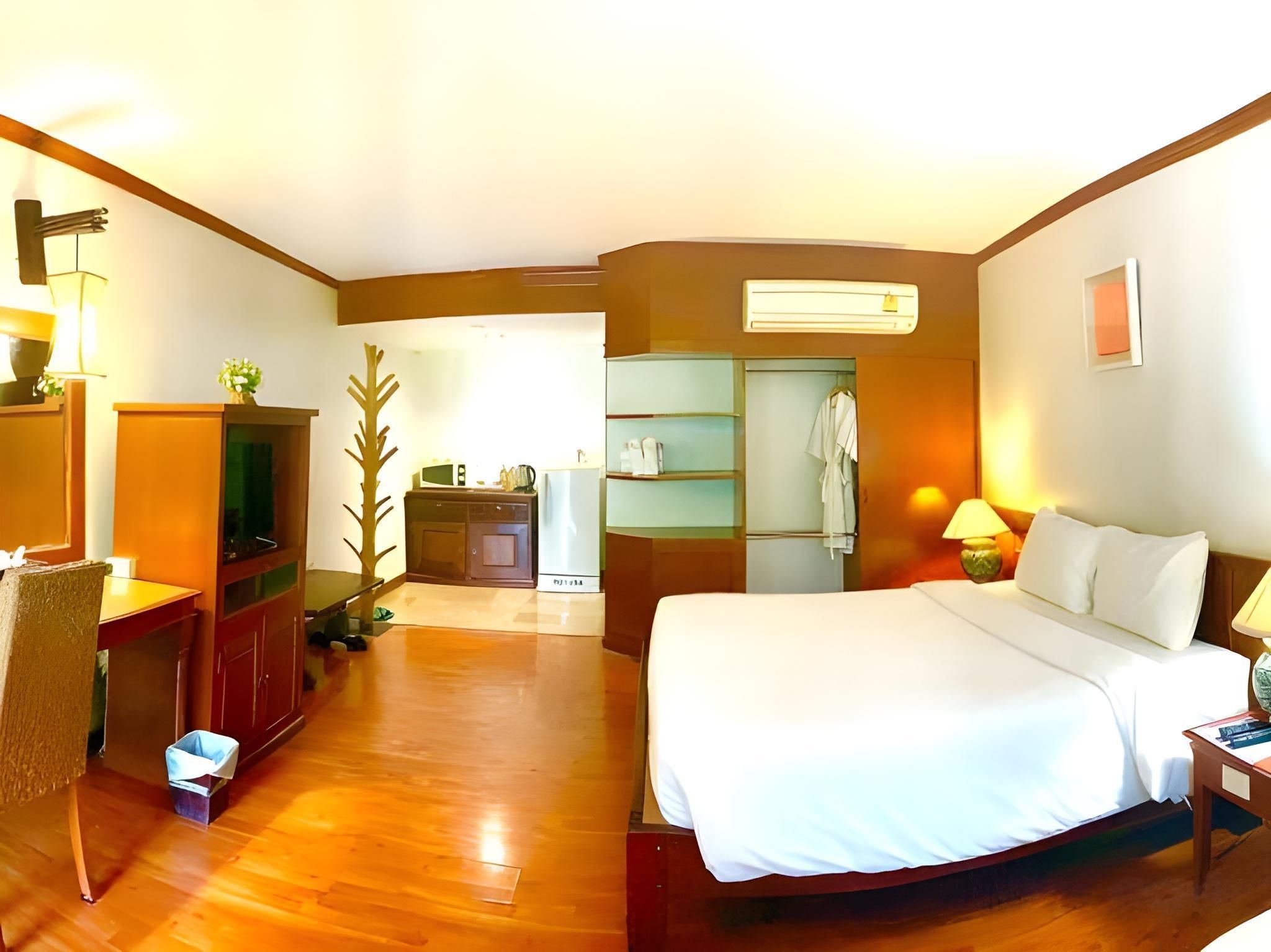 A hotel room with a bed, a desk, a chair, a TV, a wardrobe, and a bathroom visible through an open door.
