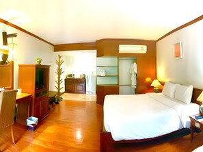 A hotel room with a bed, a desk, a chair, a TV, a wardrobe, and a bathroom visible through an open door.