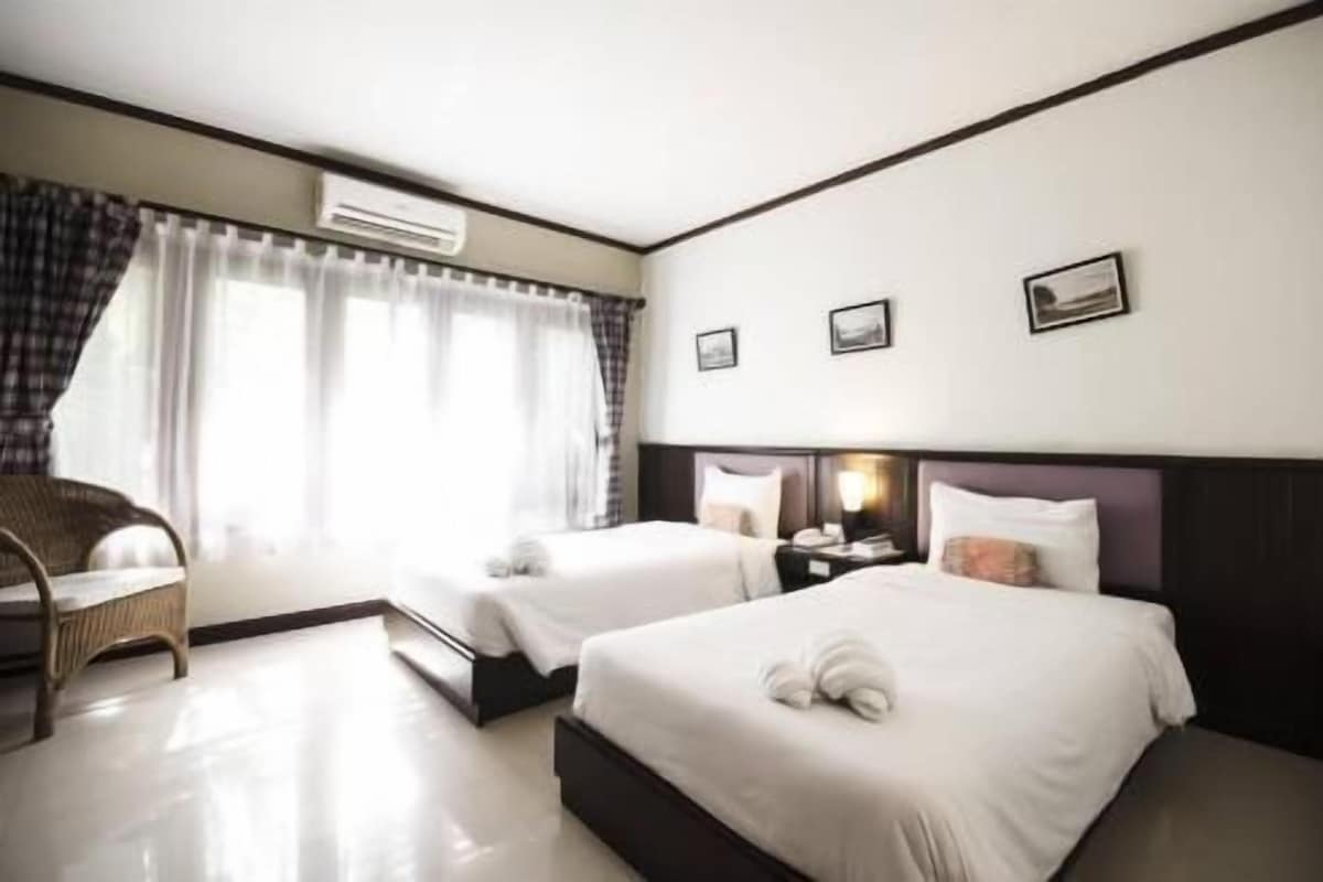 A hotel room with two beds, a chair, a nightstand, and an air conditioning unit.