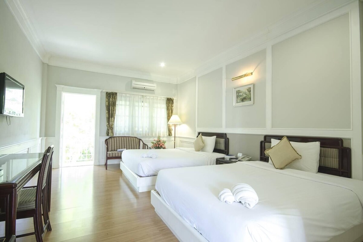A hotel room with two beds, a desk, a chair, and a television.
