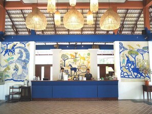 A reception desk with a blue counter, two staff members, and a large mural with animals and a dragon.
