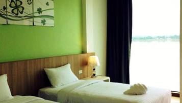 A hotel room with two beds, a nightstand, a lamp, and a view of the sea.