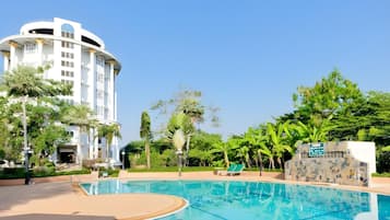 Une piscine à l’eau d’un bleu cristallin, entourée d’une végétation luxuriante et bordée d’un bâtiment moderne à la façade incurvée.