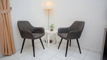 Une pièce comprenant deux fauteuils gris à revêtement en tissu, une petite table blanche avec une lampe et une plante, et un sol blanc.