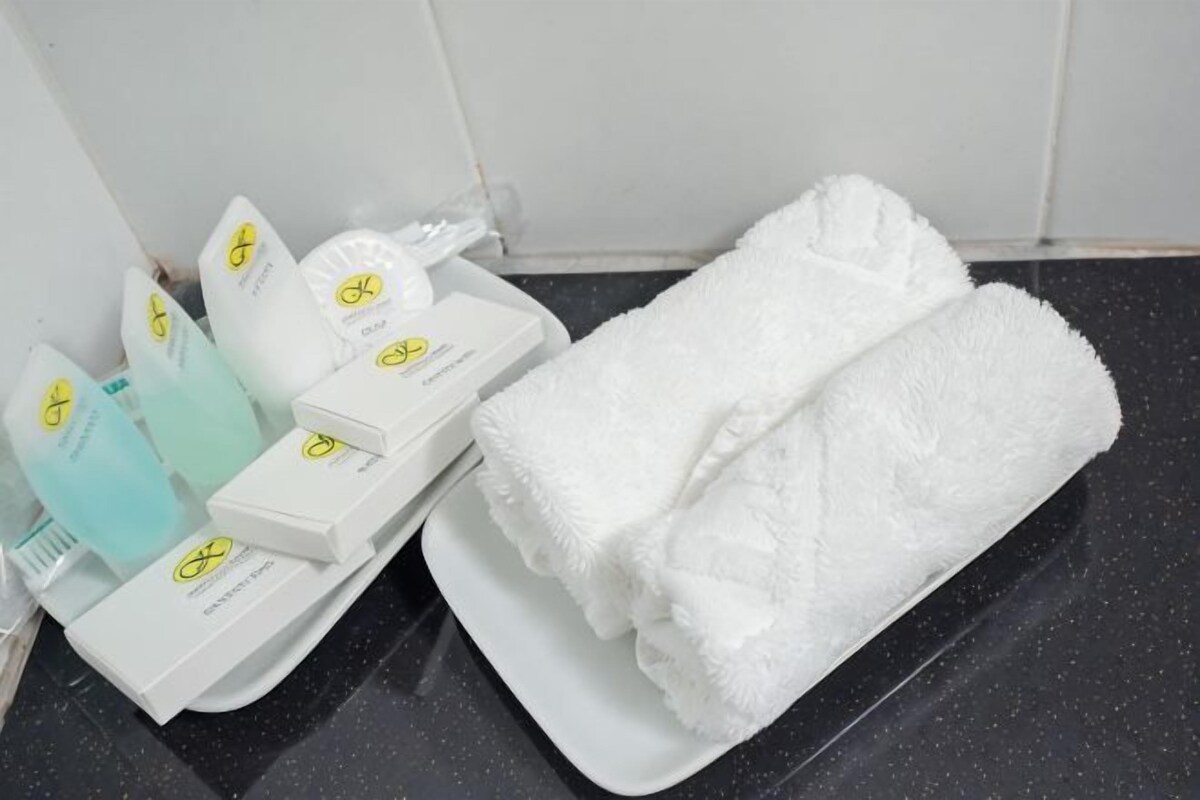 Une salle de bain avec une serviette blanche, un plateau blanc et plusieurs articles de toilette, notamment une brosse à dents, du dentifrice et un distributeur de savon.