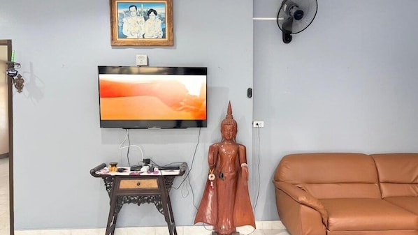 Un salon comprenant une télévision, une statue, un canapé et une petite table sur laquelle sont posés divers objets.