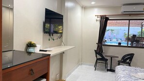 Habitació d'hotel petita amb un llit, un escriptori amb un ordinador, un televisor fixat a la paret i una finestra que dona al carrer.