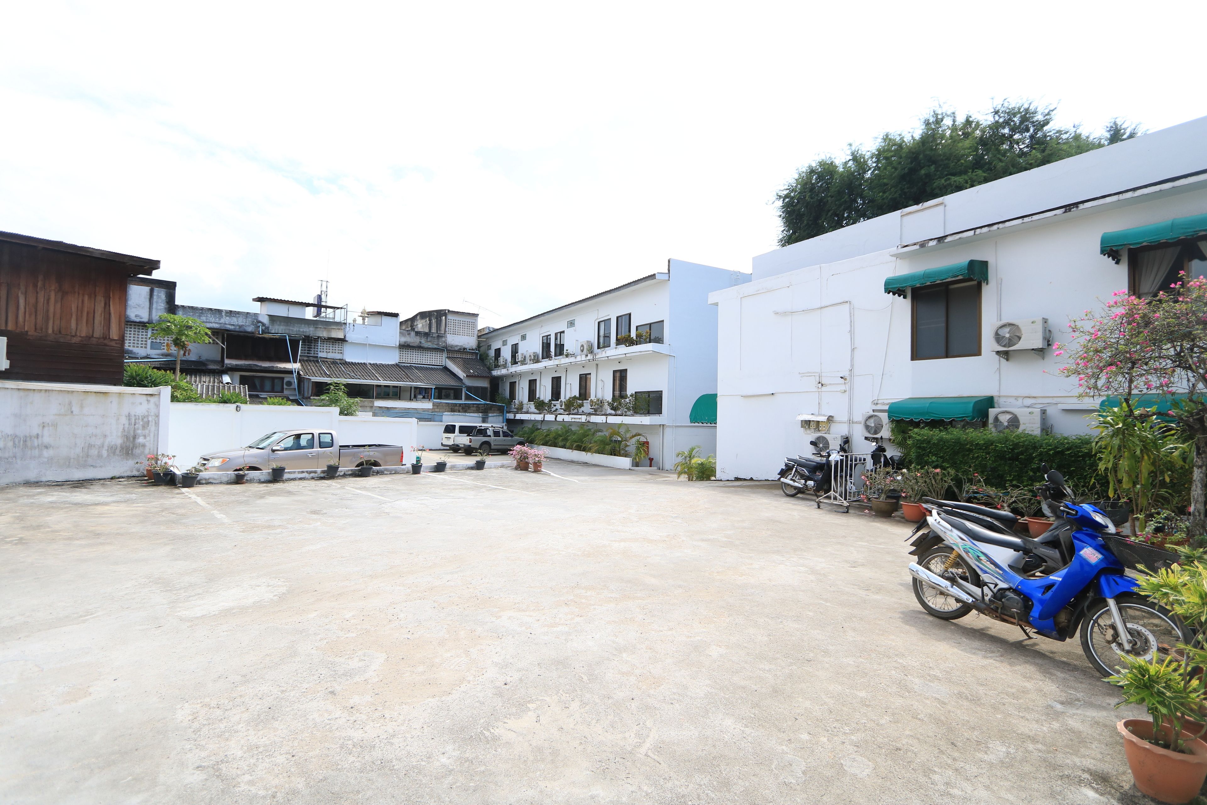 A parking area with a blue motorcycle, white buildings, and a white van.