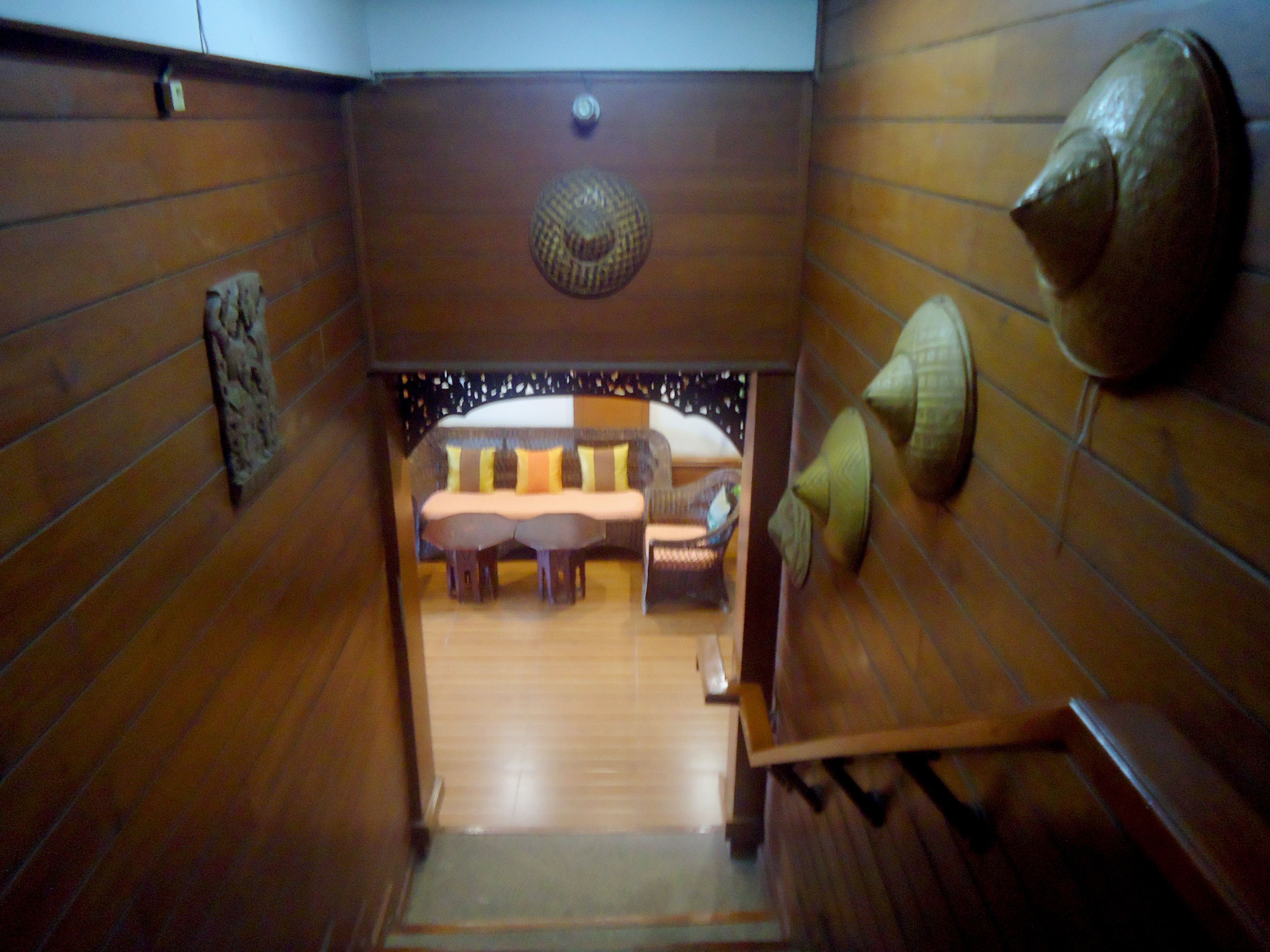 A narrow hallway leading to a room with a sofa and chairs, wooden walls, and a decorative ceiling piece.