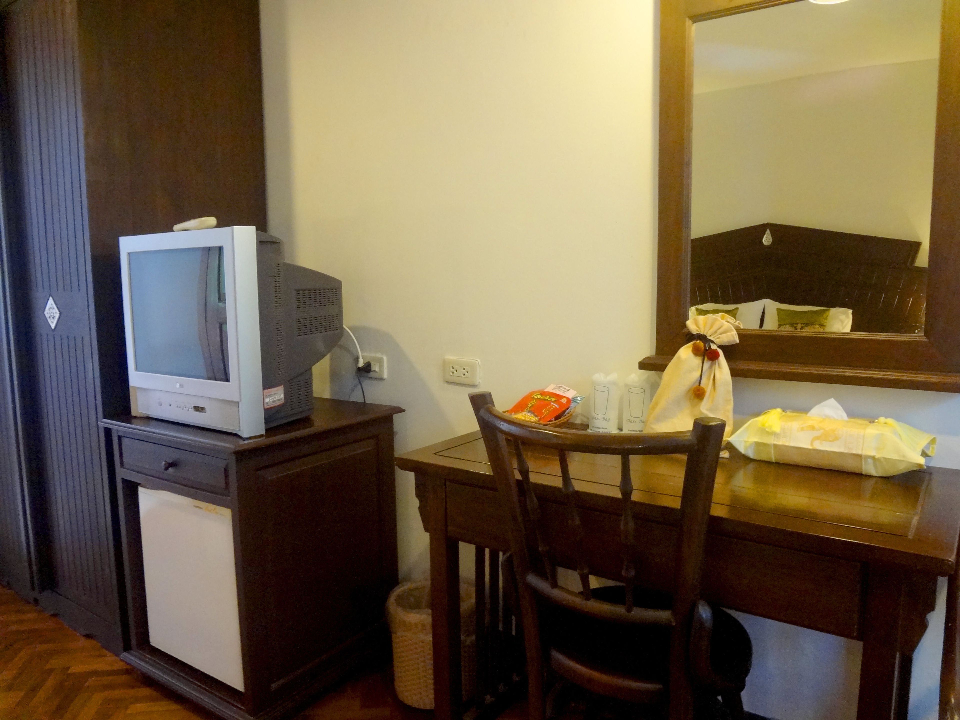 Ein kompaktes Hotelzimmer mit kleinem Fernseher auf einem Schrank, einem Holztisch mit Stuhl und einem Spiegel über dem Tisch.