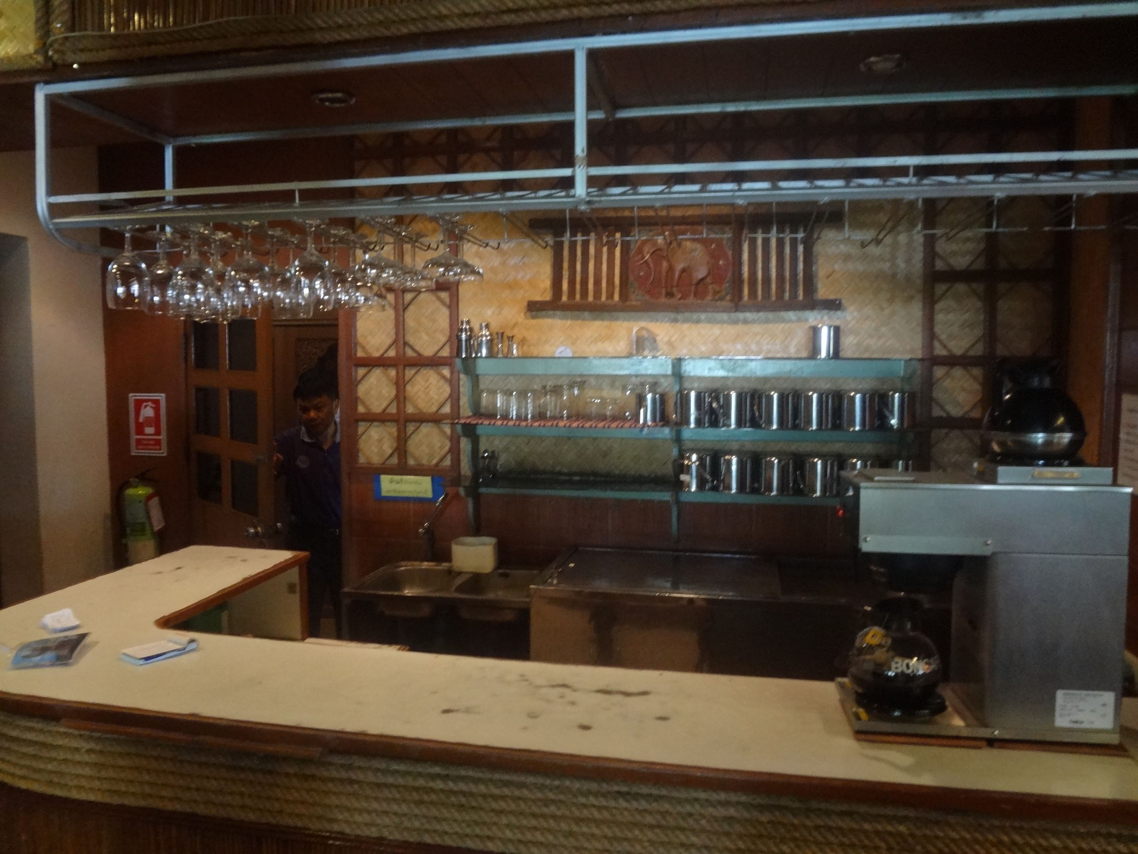 Eine Bar mit Regalen voller Gläser und Flaschen, einer Theke mit Unterlagen und einem Feuerlöscher.