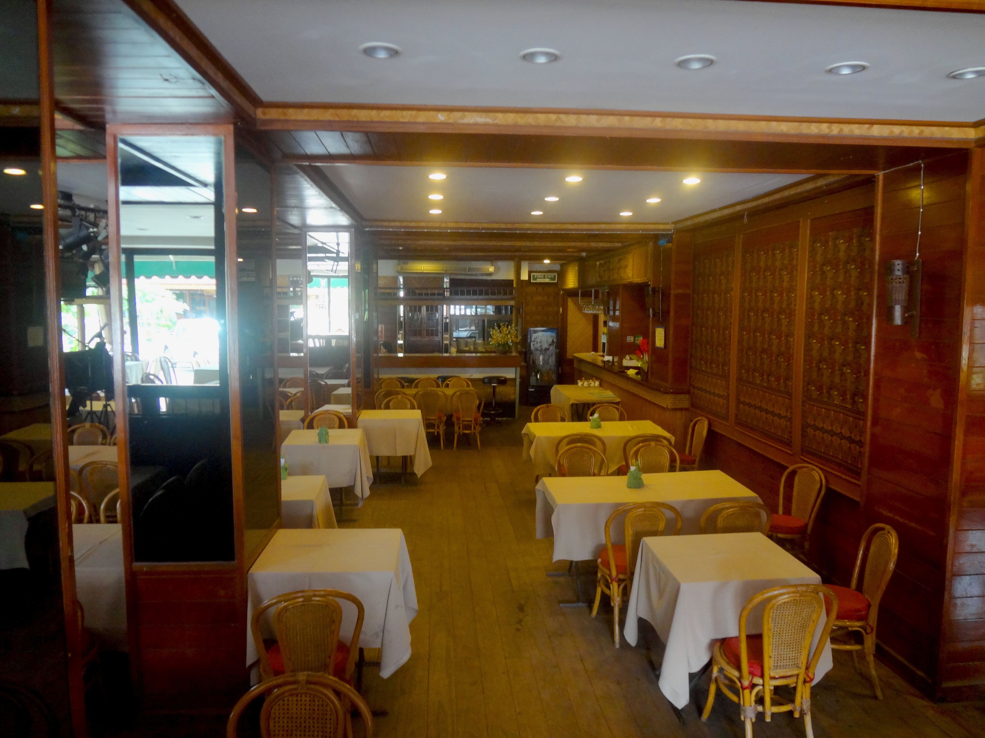 A restaurant interior with multiple tables and chairs, wooden flooring, and a bar area.