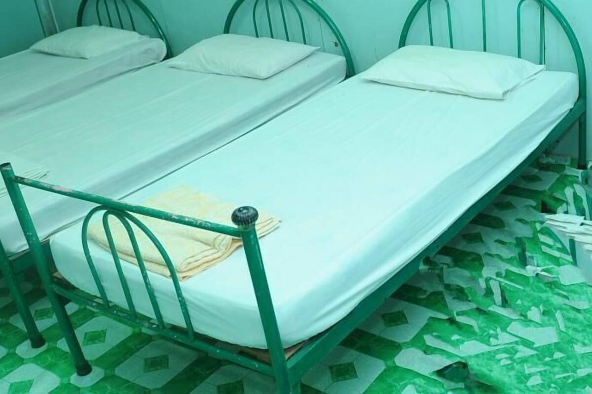 Une chambre avec deux lits simples, chacun doté d’une structure métallique verte et de draps blancs. Le sol est recouvert de carreaux aux motifs verts et blancs.