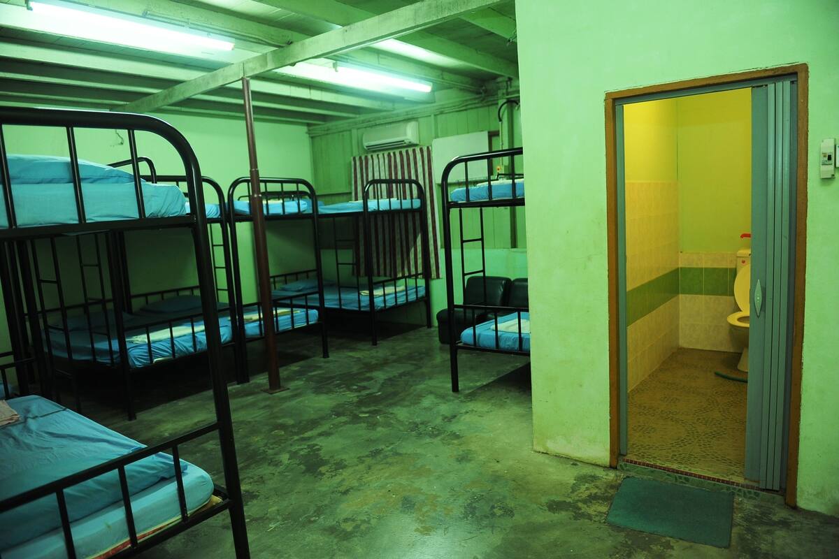 Une chambre de dortoir avec des lits superposés, une salle de bain avec des toilettes et une porte donnant sur une autre pièce.