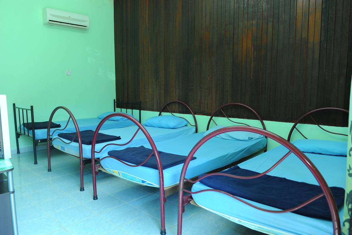Une chambre de dortoir avec quatre lits en métal, chacun étant équipé de draps bleus et d’une couverture bleu foncé.