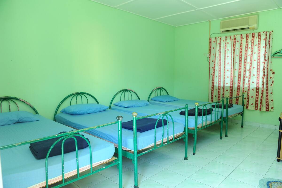 Une chambre de dortoir avec quatre lits superposés, des structures métalliques vertes et du linge de lit bleu.