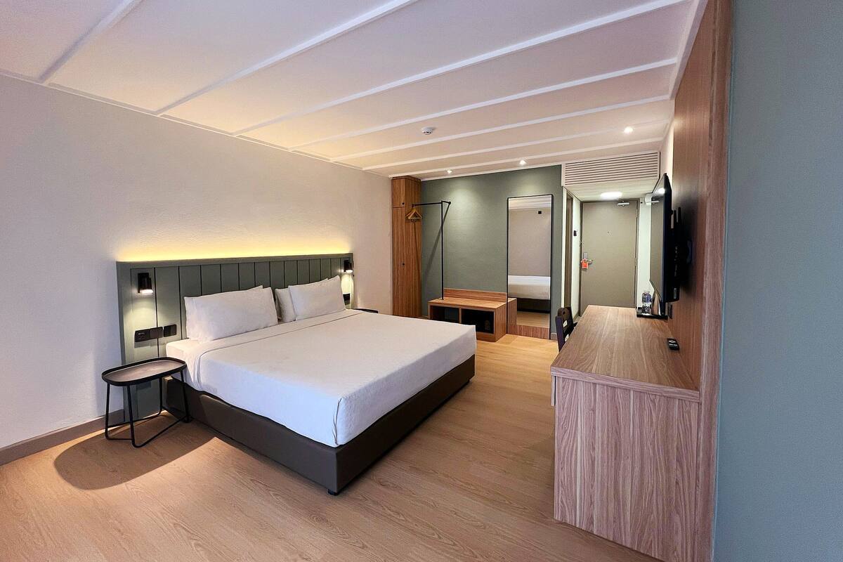 A modern hotel room with a large bed, bedside table, mirror, and a TV mounted on the wall.
