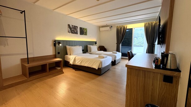 Une chambre d’hôtel avec deux lits, un banc en bois, une petite table et une poubelle.