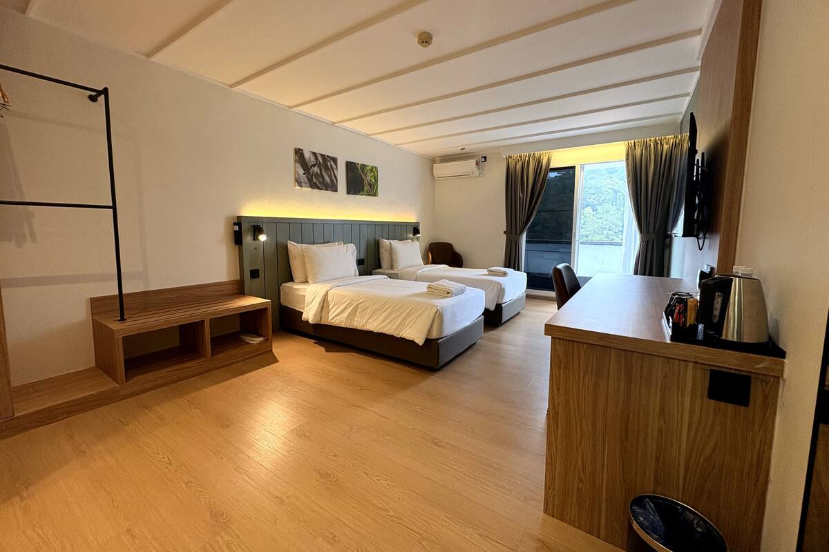 A hotel room with two beds, a wooden bench, a small table, and a trash bin.