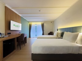 Quarto de hotel com cama, escrivaninha, cadeira, televisão e janela com cortinas.