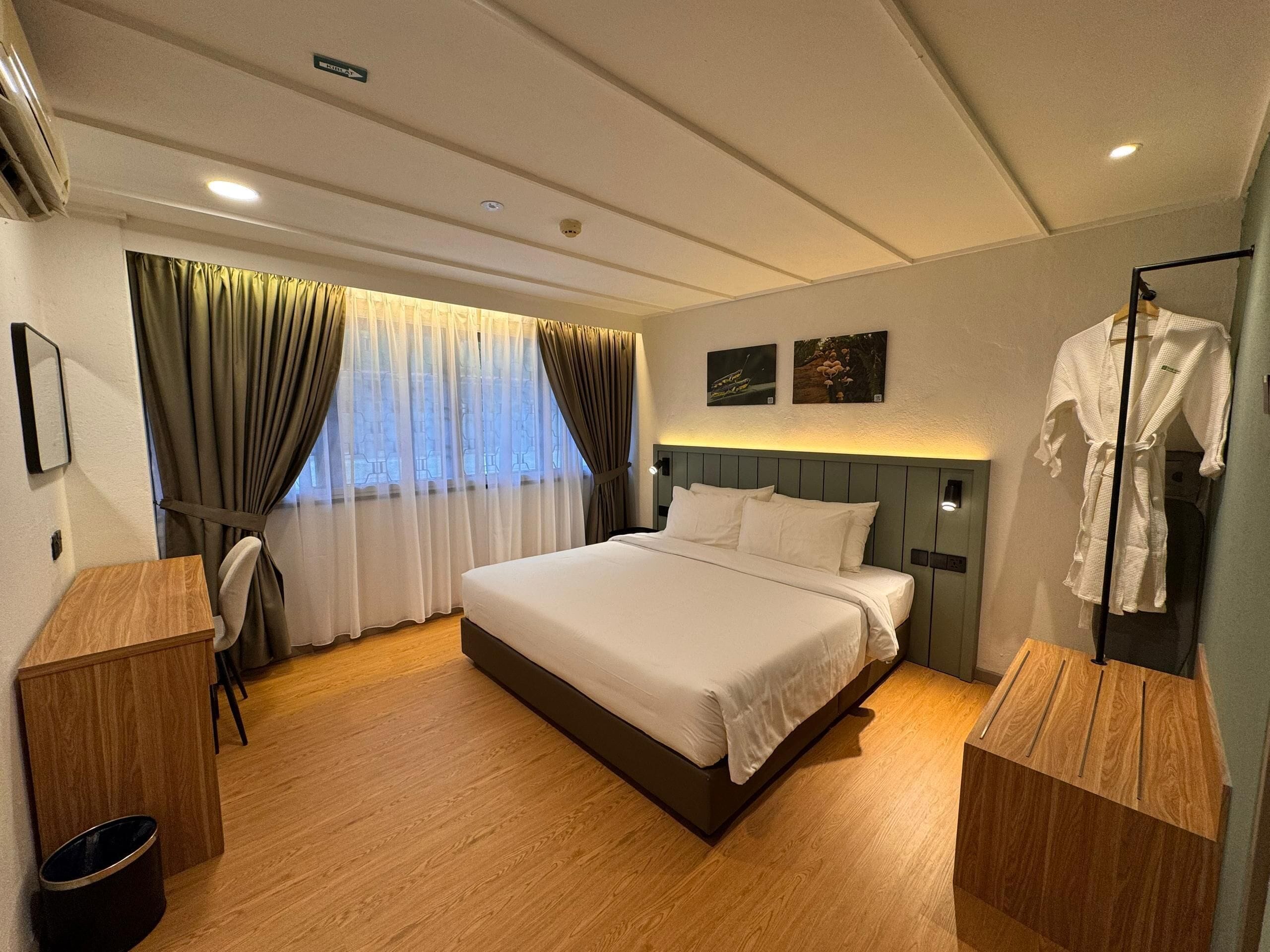 Een hotelkamer met een groot bed, houten vloer, een bureau en een stoel.