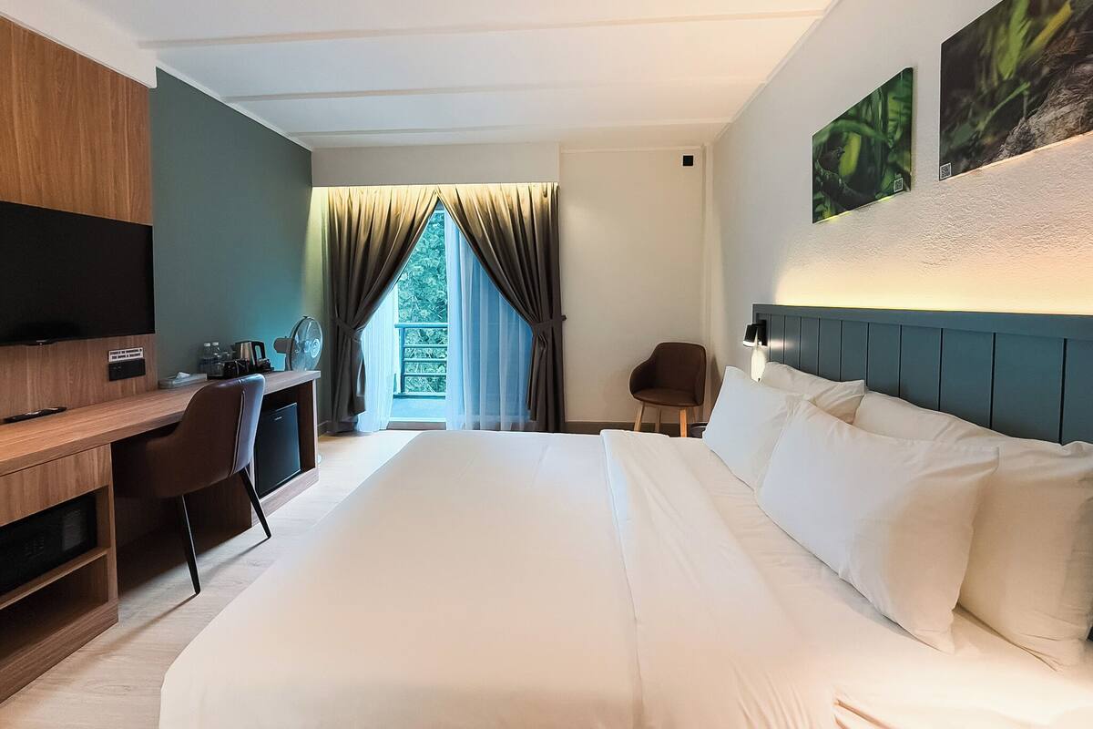 A hotel room with a large bed, a desk with a chair, a television, and a window with curtains.