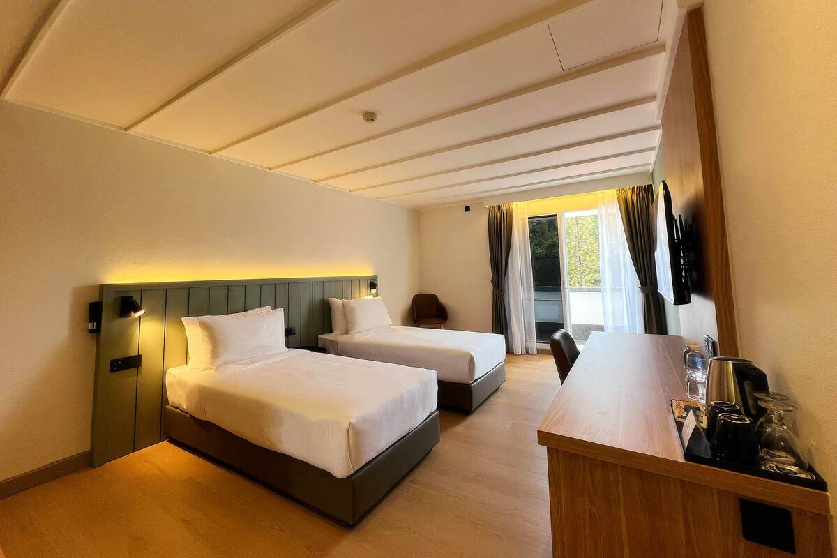A hotel room with two beds, a desk, and a window with curtains.