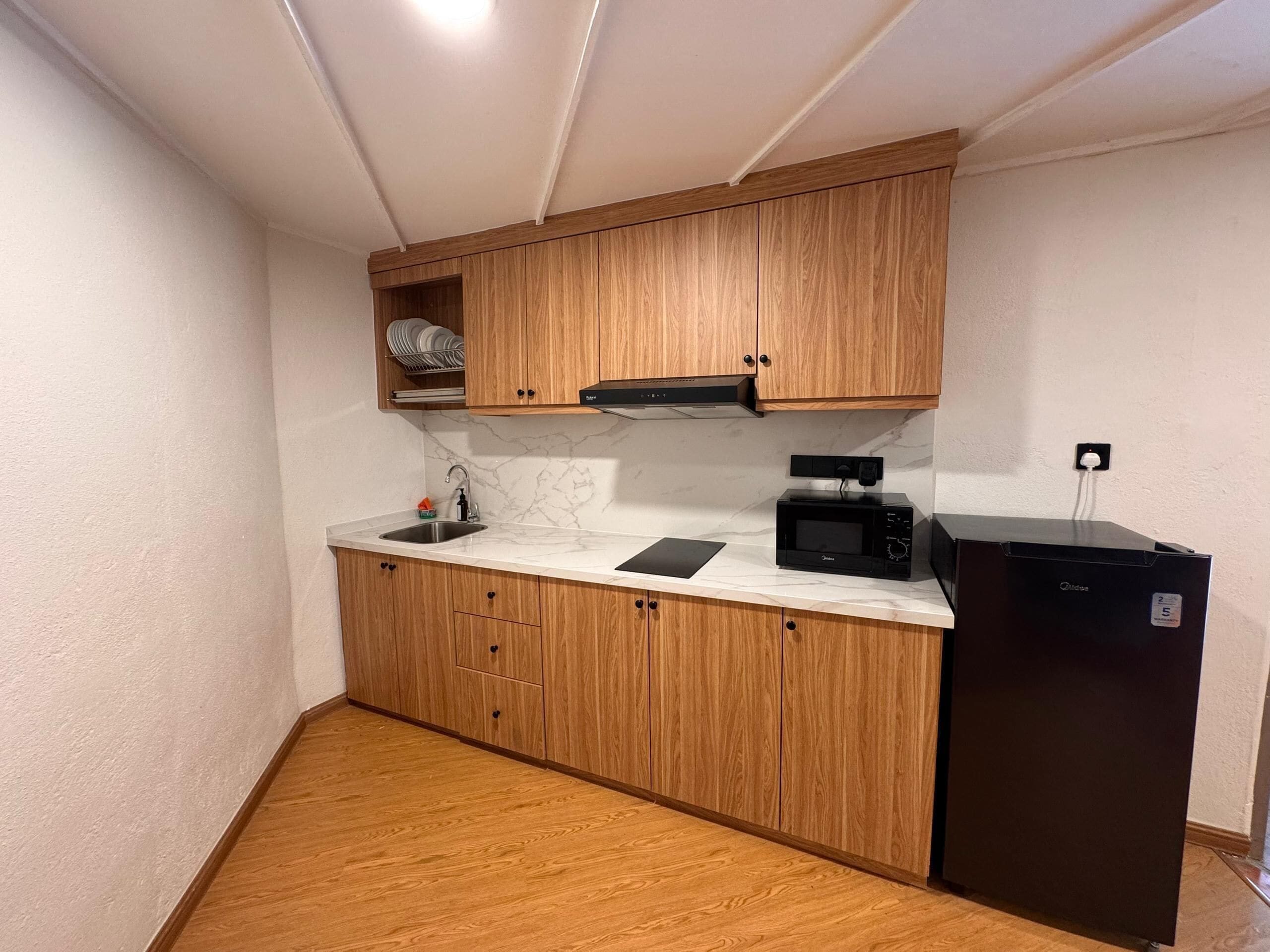 A compact kitchen with wooden cabinets, a built-in microwave, and a black refrigerator.