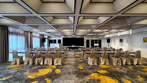 Une salle de conférence dotée d’un grand écran, de rangées de chaises et d’un tapis aux motifs jaunes et noirs.