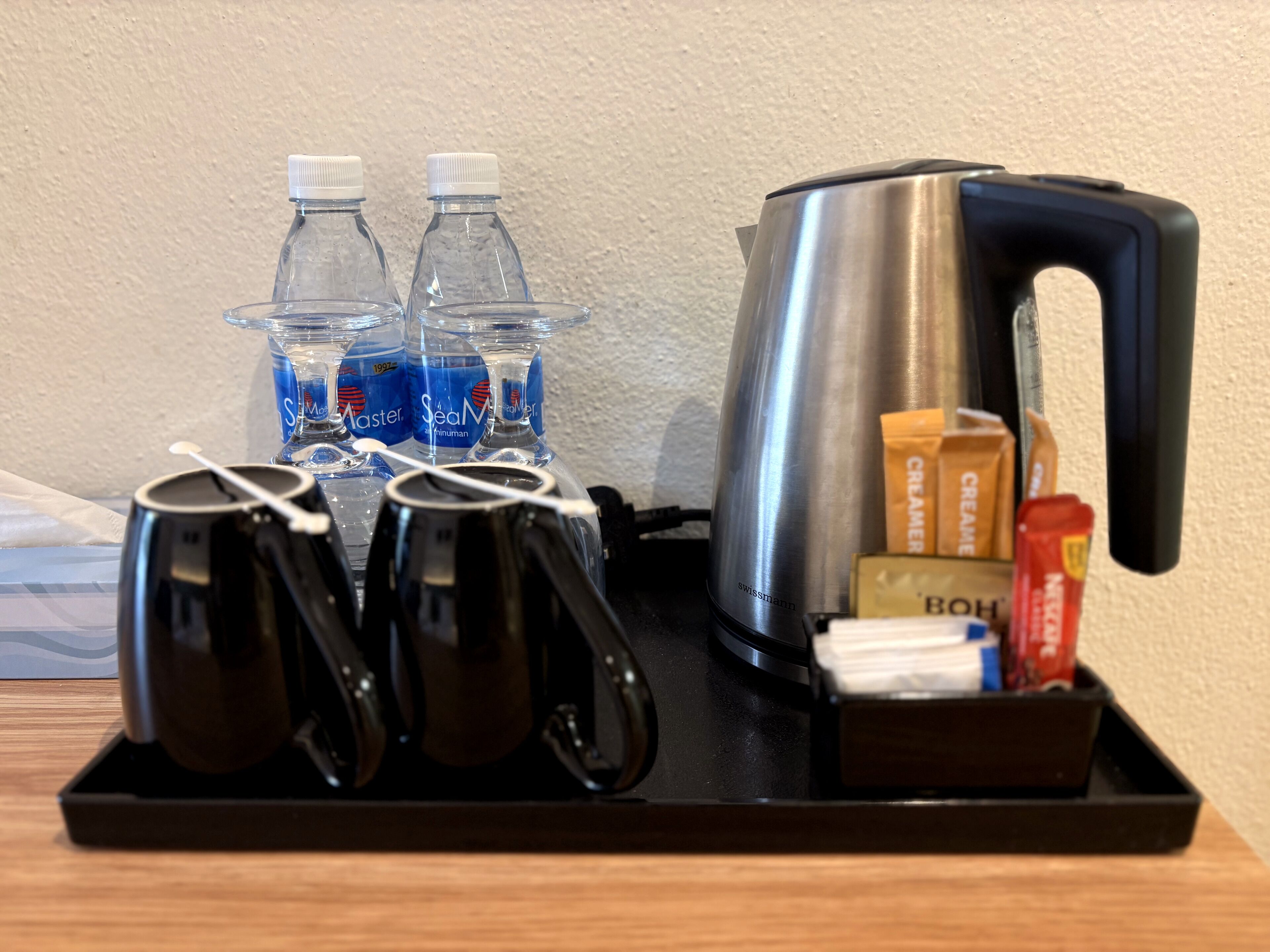 A tray with a kettle, four mugs, two bottles of water, and some condiments.