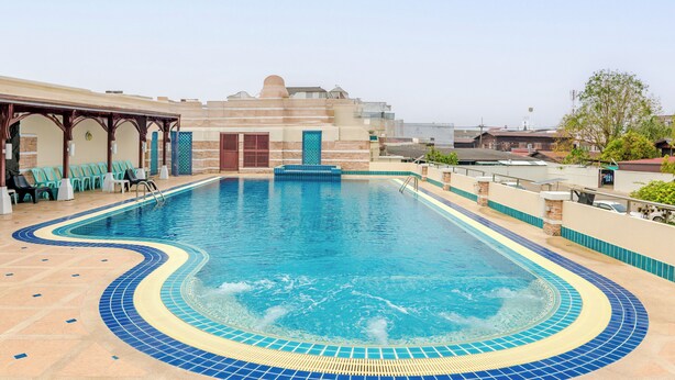 A swimming pool with a tiled edge, lounge chairs, and a covered seating area. - Dhevaraj Hotel (Nan)