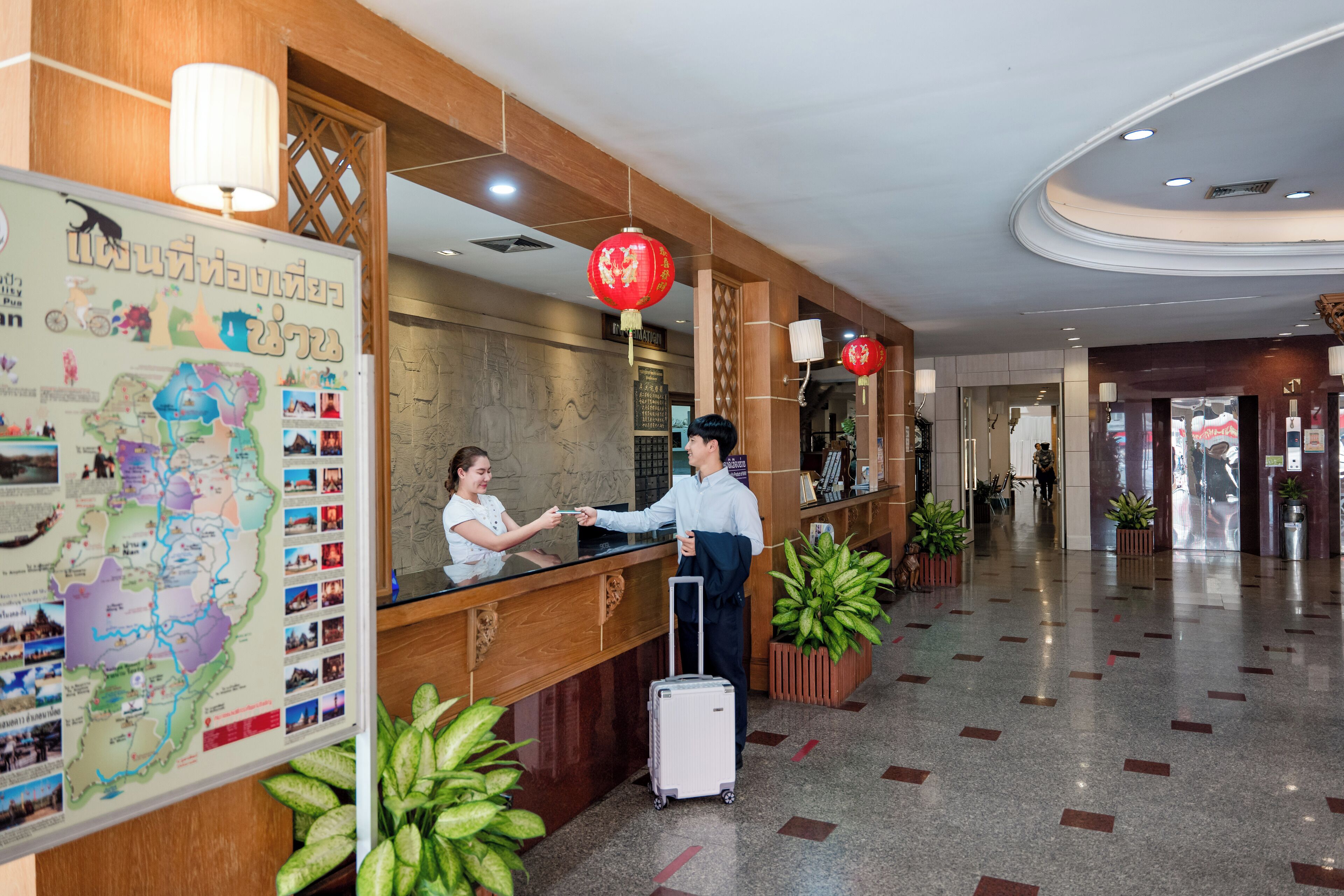A hotel reception area with a wooden reception desk, a map on the wall, and red lanterns.