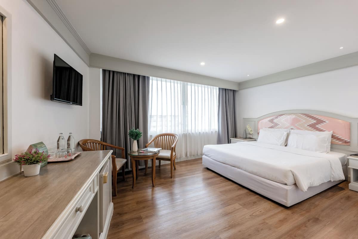 Ein Hotelzimmer mit einem Bett, einem Schreibtisch mit Stuhl, einem Fernseher und einem Fenster mit Vorhängen.