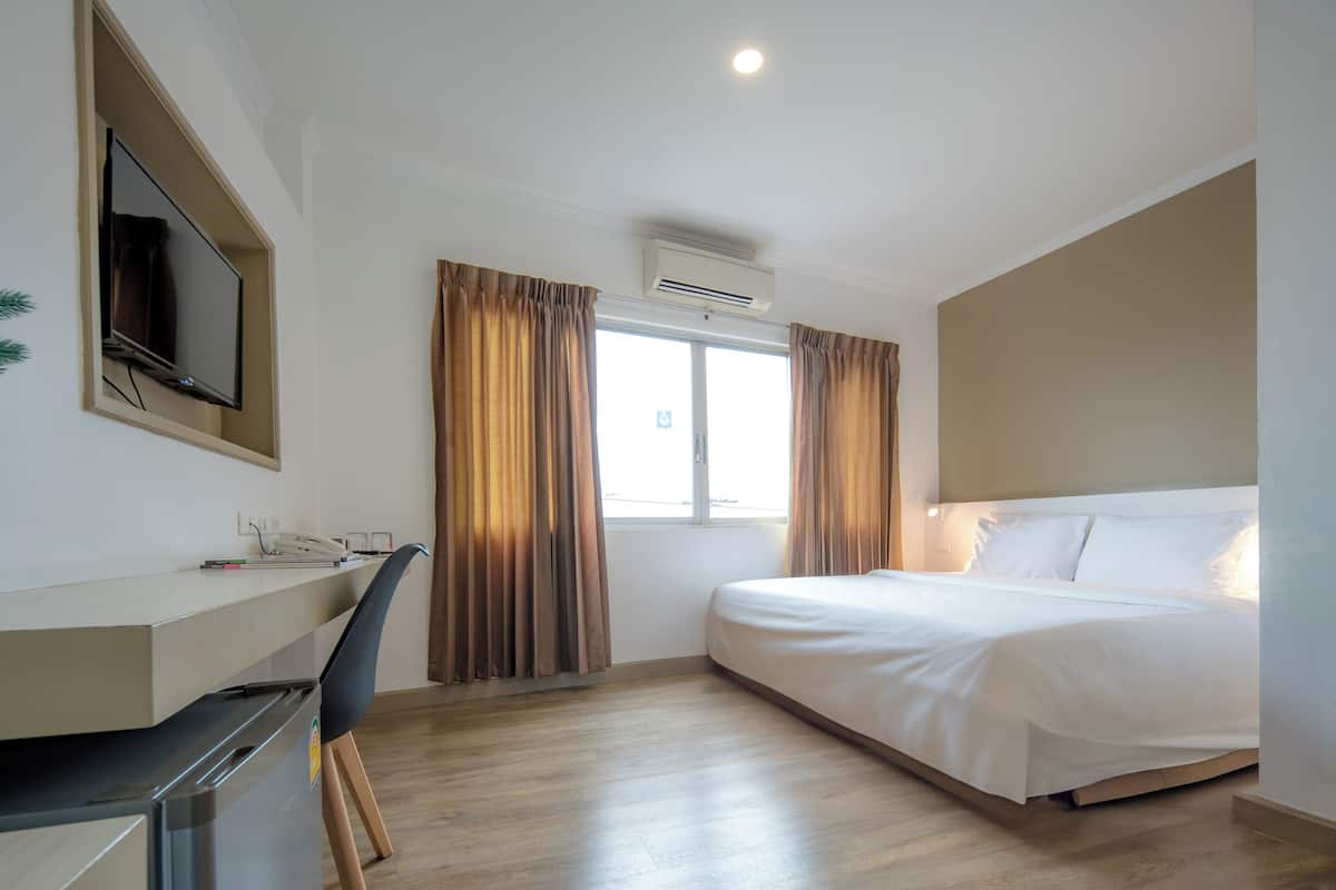Ein Hotelzimmer mit einem Bett, einem Schreibtisch mit Stuhl, einem Fernseher und einer Klimaanlage.