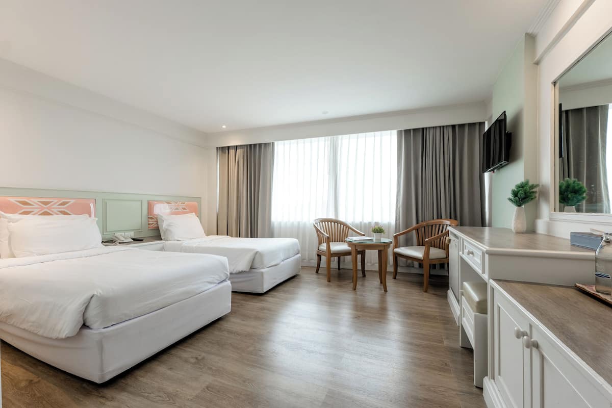 Ein Hotelzimmer mit zwei Betten, einem kleinen Tisch mit Stühlen, einem Fernseher und einem großen Fenster mit Vorhängen.